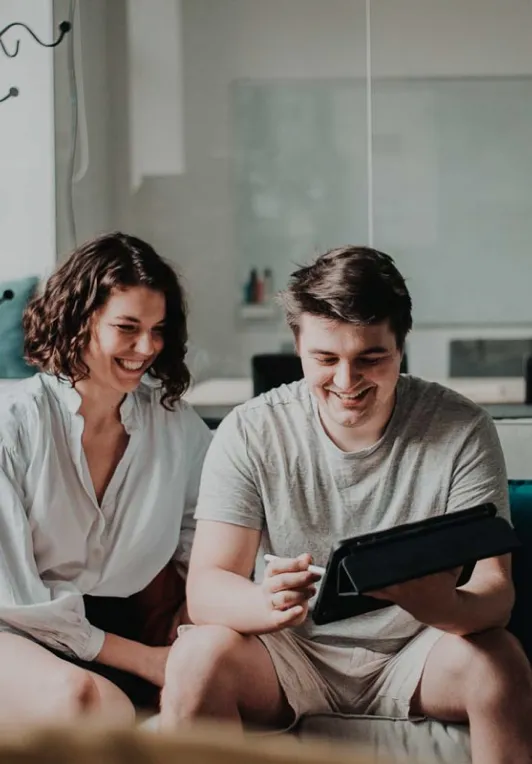 A man and woman sitting on a couch looking at a tablet.